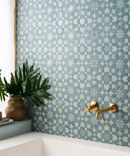 Bathroom corner with geometric patterned tiles, gold faucet, and plant