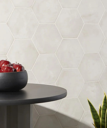 Hexagonal tiles on a wall with a bowl of apples and a plant on a table.