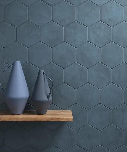 Two gray vases on a wooden shelf against a dark hexagonal tiled wall.