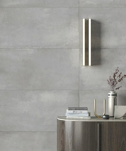 Modern bathroom setting with a wall-mounted light fixture, books, and decorative items against a gray tiled wall.