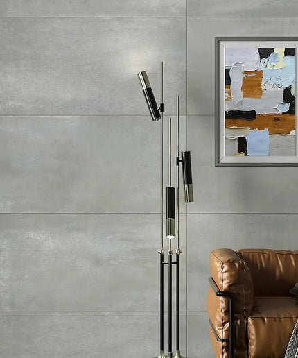 Modern floor lamp with abstract art on a gray wall above a brown sofa.