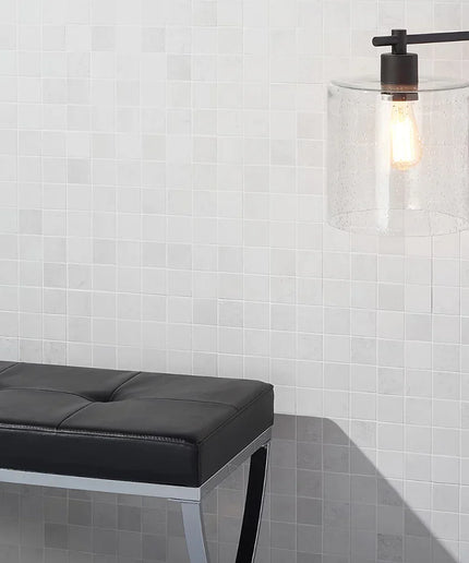 Modern black floor lamp with clear glass shade against a white tiled wall.