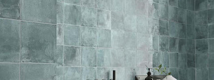 Teal tiled wall with a small plant and decorative item on a ledge.