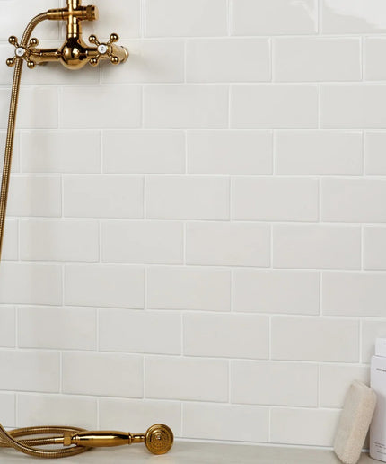Gold shower head and hose against a white tiled wall