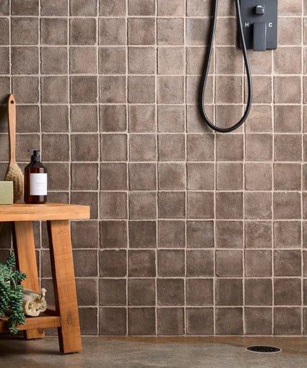 Brown tiled wall with a wooden shelf and plants in a bathroom setting