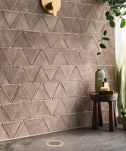 Bathroom with geometric triangle-patterned tiles, a small table with bottles, and a plant.
