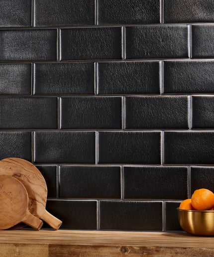 Black tiled wall with wooden cutting boards and a bowl of oranges on a wooden surface