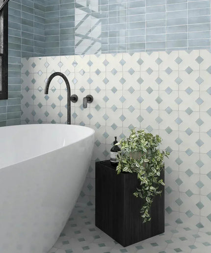 Bathroom with a white freestanding bathtub against a tiled wall with geometric pattern.