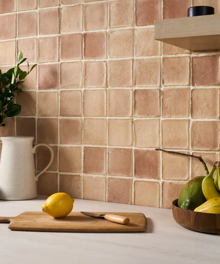 Kitchen counter with a lemon, cutting board, and bowl of fruit against a tiled wall.