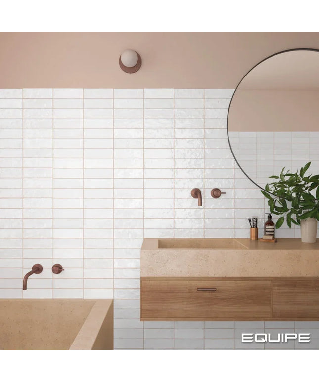 Bathroom interior with wooden vanity, round mirror, and tiled wall.