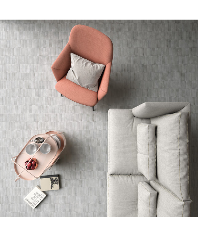 A top-down view of a modern living room corner featuring a dusty pink armchair with a light gray pillow, a light gray sofa, and a matching pink side table holding a tray with cups and a small decorative object, all set on a gray textured tile floor.