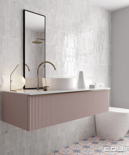 A modern floating bathroom vanity in a dusty pink ribbed finish, paired with a white vessel sink, a white marble countertop, and a tall black-framed mirror. The bathroom features textured light gray tiles, a white wall, and a patterned tile floor, with a window on the right.