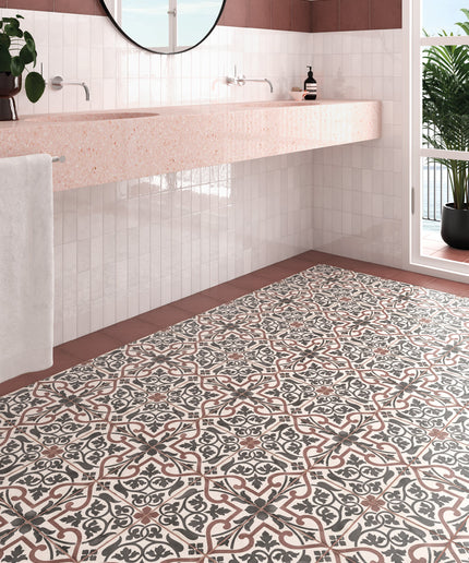 A bathroom interior showing a patterned ceramic floor tile with a classic French tile design in beige, brown, and gray, alongside a pink countertop and white subway tiles.