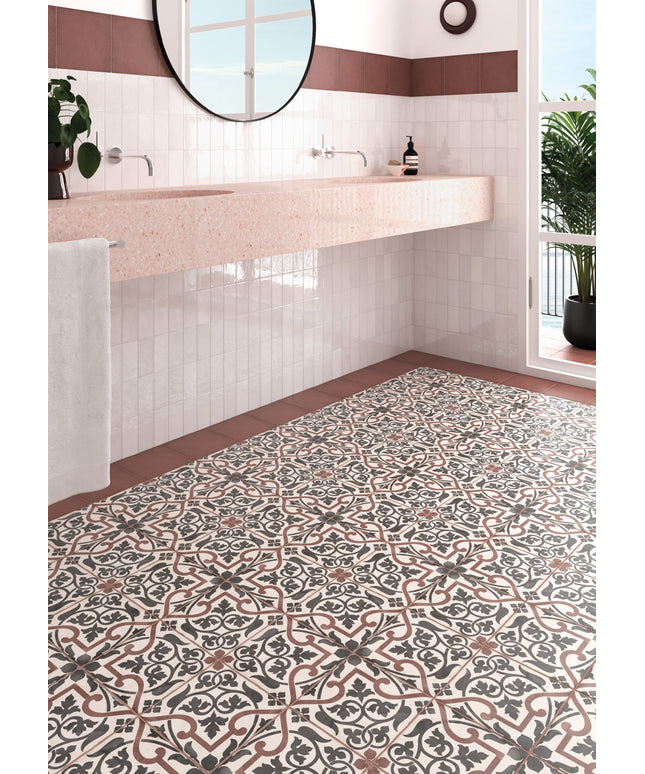 A bathroom interior showing a patterned ceramic floor tile with a classic French tile design in beige, brown, and gray, alongside a pink countertop and white subway tiles.