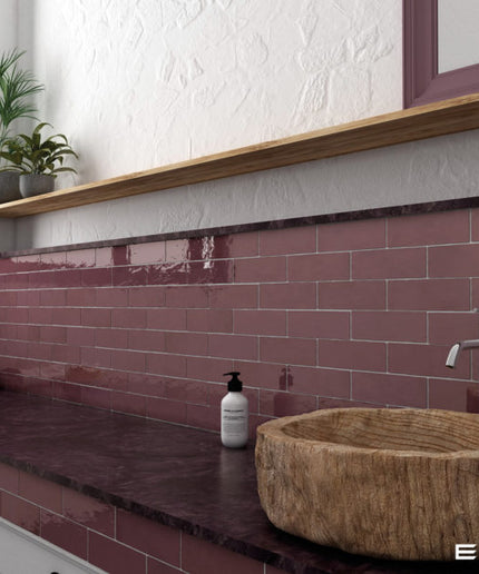 A bathroom vanity setup featuring glossy terracotta pink subway tiles, a dark stone countertop, a round natural wood vessel sink, and a white wall with a wooden shelf and plant.