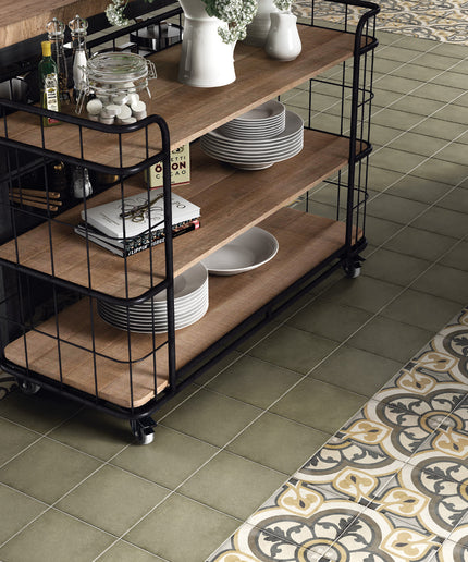 A three-tier rolling utility cart with a black metal frame and light brown wooden shelves, styled in a kitchen setting with plates, vases, and kitchenware on a tiled floor.
