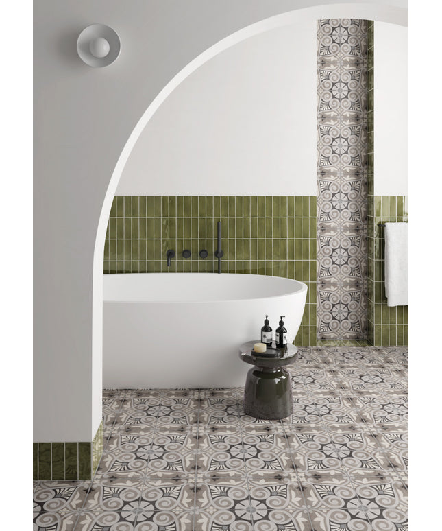 A styled bathroom interior featuring a white freestanding bathtub set within a white arched alcove, surrounded by olive green square tiles and patterned gray-and-white floor and wall tiles.