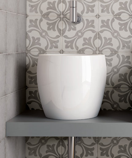A glossy white ceramic vessel sink sits on a gray floating shelf against a wall of gray and white patterned tiles.