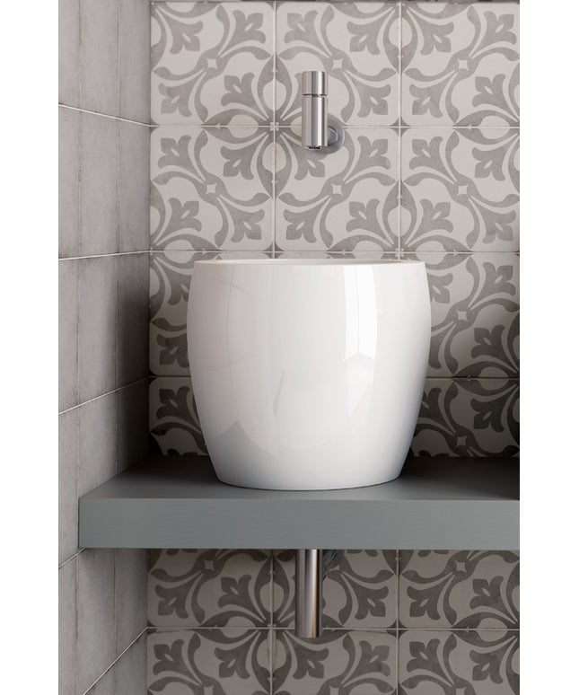 A glossy white ceramic vessel sink sits on a gray floating shelf against a wall of gray and white patterned tiles.