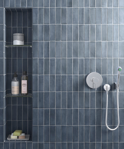 A modern shower wall with dark blue-gray rectangular tiles, a built-in niche with shelves and toiletries, and a chrome shower fixture with a handheld shower head.