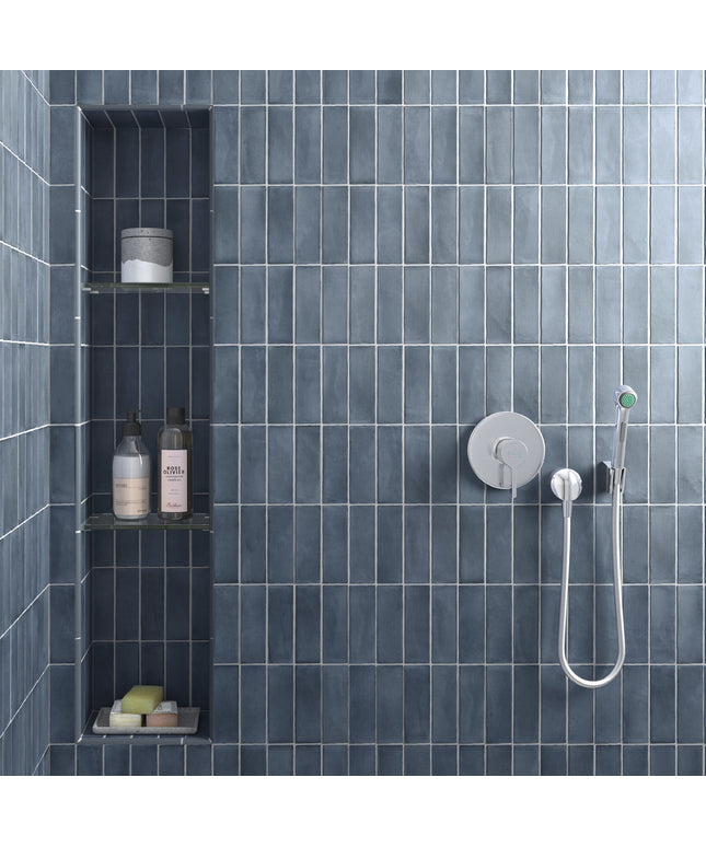 A modern shower wall with dark blue-gray rectangular tiles, a built-in niche with shelves and toiletries, and a chrome shower fixture with a handheld shower head.