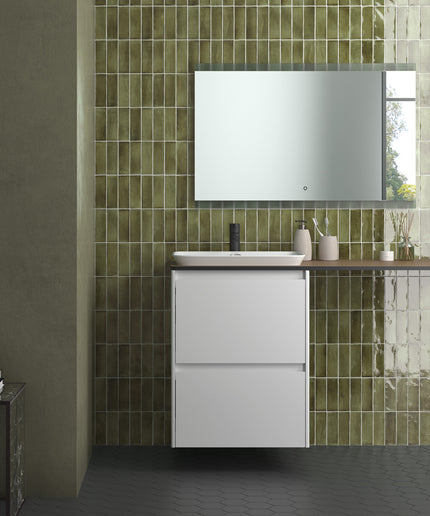 A modern bathroom vanity setup with a white two-drawer cabinet, a white rectangular basin, a dark wood-look countertop, a wall-mounted mirror, and glossy green tile wall behind it.