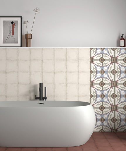 A modern freestanding oval bathtub in matte white, set against a tiled bathroom wall with a patterned tile section on the right, a small white stool, and minimalist wall decor.