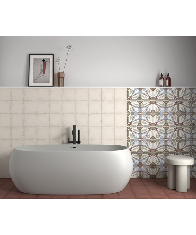 A modern freestanding oval bathtub in matte white, set against a tiled bathroom wall with a patterned tile section on the right, a small white stool, and minimalist wall decor.