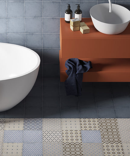 A modern bathroom scene showing a terracotta floating vanity with a white bowl sink, dark soap dispensers, and a navy towel, next to a white freestanding tub and a patchwork tile floor.