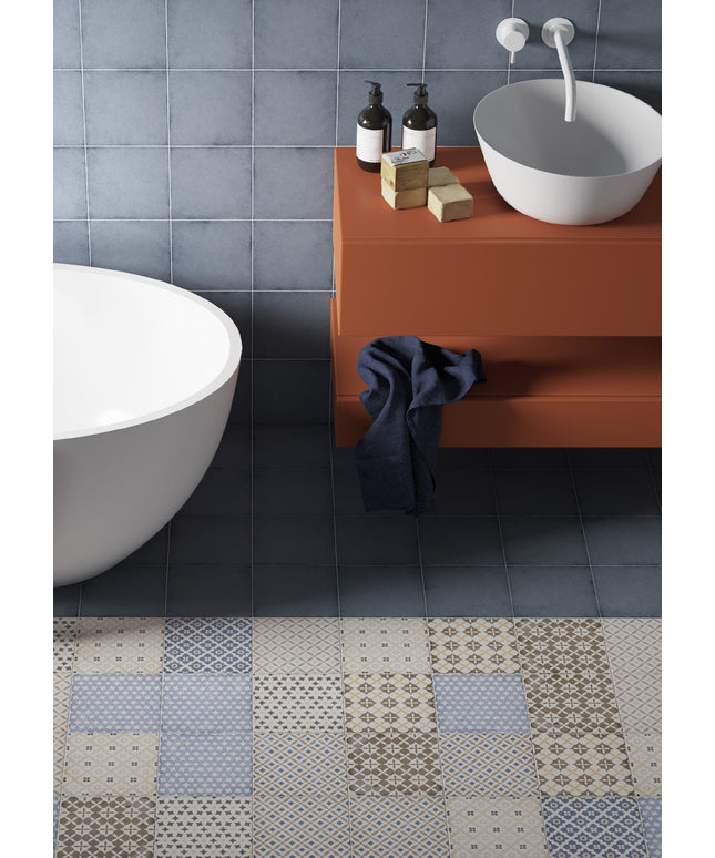 A modern bathroom scene showing a terracotta floating vanity with a white bowl sink, dark soap dispensers, and a navy towel, next to a white freestanding tub and a patchwork tile floor.