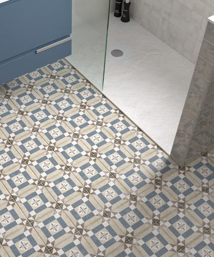 Blue, beige, and white patterned ceramic floor tiles installed in a modern bathroom, shown alongside a glass shower door and light gray tiled walls.