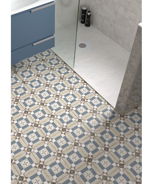Blue, beige, and white patterned ceramic floor tiles installed in a modern bathroom, shown alongside a glass shower door and light gray tiled walls.