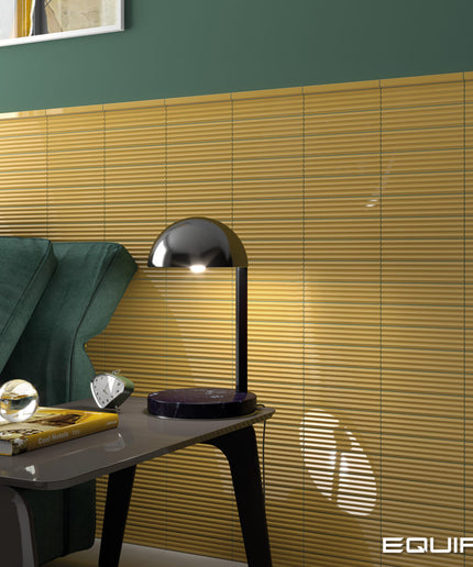 A modern black dome-shaped table lamp sits on a dark side table next to a green sofa, with a wall of horizontal wood slats behind it. The word EQUIPE appears in the bottom right corner.