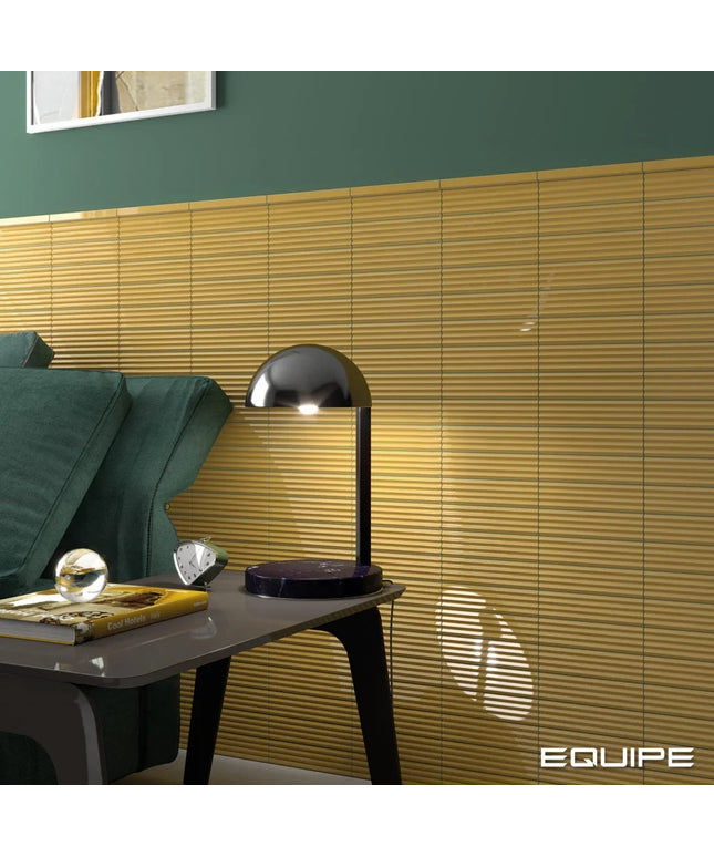 A modern black dome-shaped table lamp sits on a dark side table next to a green sofa, with a wall of horizontal wood slats behind it. The word EQUIPE appears in the bottom right corner.