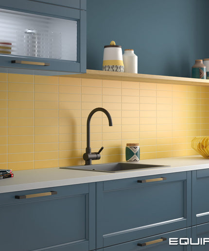 A modern kitchen scene with slate blue cabinets, a yellow subway tile backsplash, a black gooseneck faucet, and white countertops. The word EQUIPE appears in the bottom right corner.