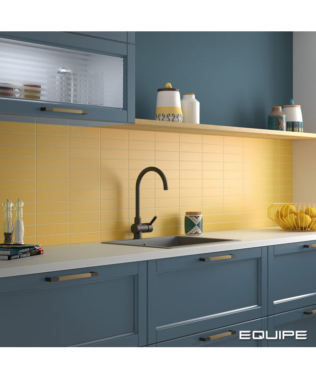 A modern kitchen scene with slate blue cabinets, a yellow subway tile backsplash, a black gooseneck faucet, and white countertops. The word EQUIPE appears in the bottom right corner.