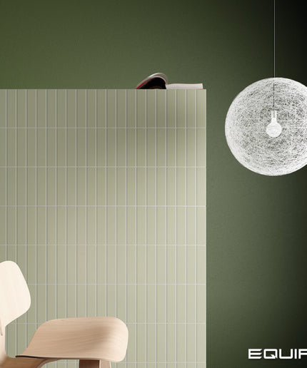 A modern interior scene with a dark olive green wall, a white spherical woven pendant light hanging on the right, a light wood chair at lower left, and a large white slatted panel behind the chair. The word EQUIPE appears in the bottom right corner.