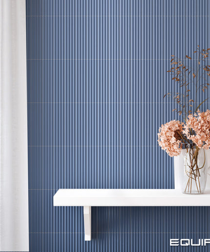 Blue ribbed wall paneling with a white floating shelf and vase of dried flowers, shown in a styled interior setting with the brand name EQUIPE in the bottom right corner.