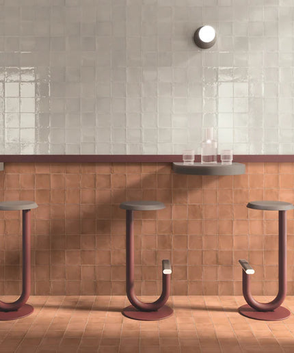 Modern bar stools against a tiled wall with a glass of water on a shelf.