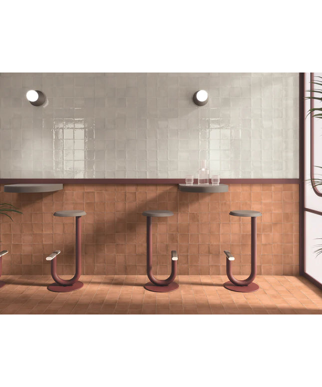 Modern bar stools against a tiled wall with a glass of water on a shelf.