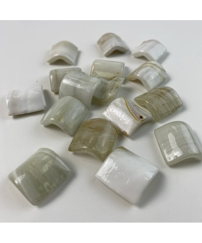 Glossy curved mosaic tile pieces in shades of white and beige on white background