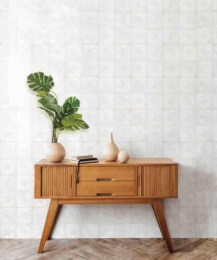 White square wall tiles behind mid-century wood console with vases and green plant.