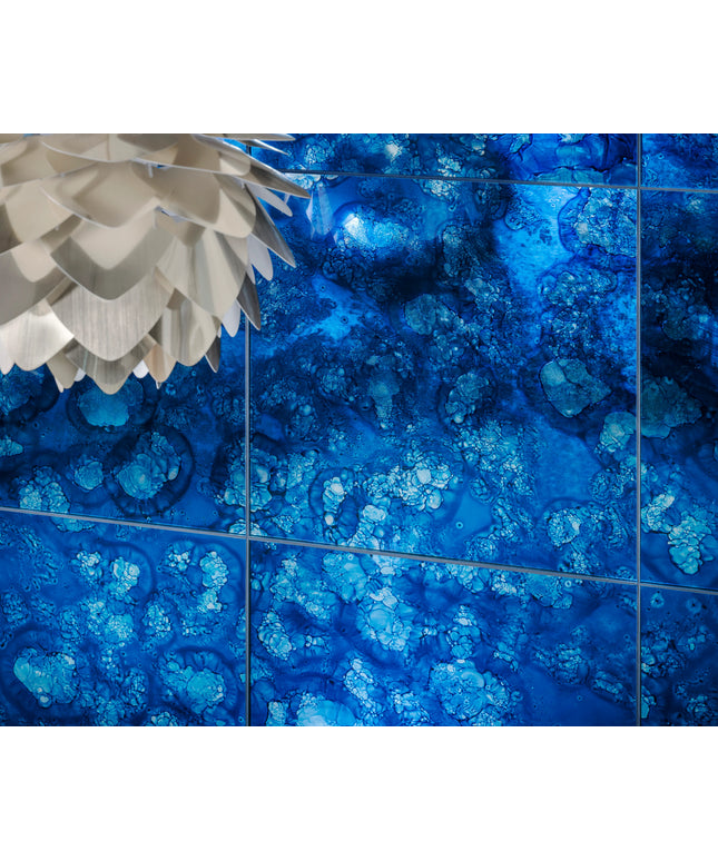Blue patterned glass tiles with a bubbly, crystalline design, shown in a grid layout with dark grout lines. A white textured pendant light is partially visible in the top-left corner.