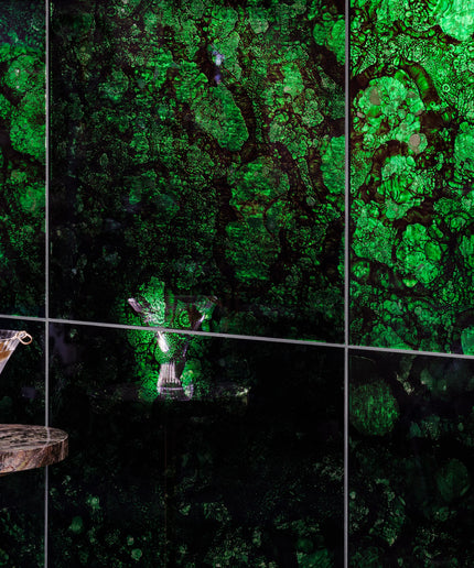 A wall-mounted multi-panel display featuring a vivid green and black marbled or cellular pattern, with a small round table and a martini glass placed in the lower left foreground.