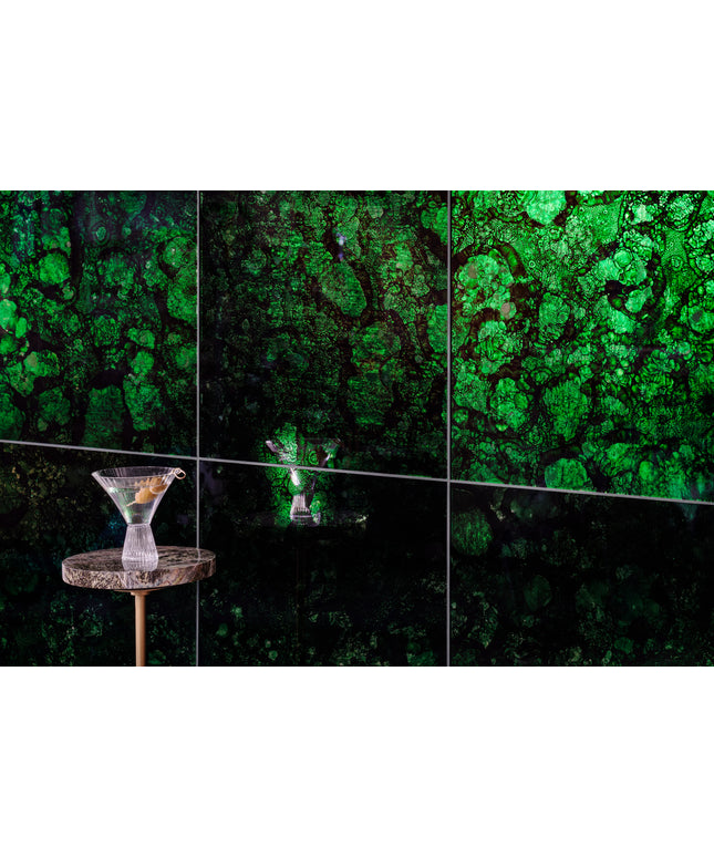 A wall-mounted multi-panel display featuring a vivid green and black marbled or cellular pattern, with a small round table and a martini glass placed in the lower left foreground.