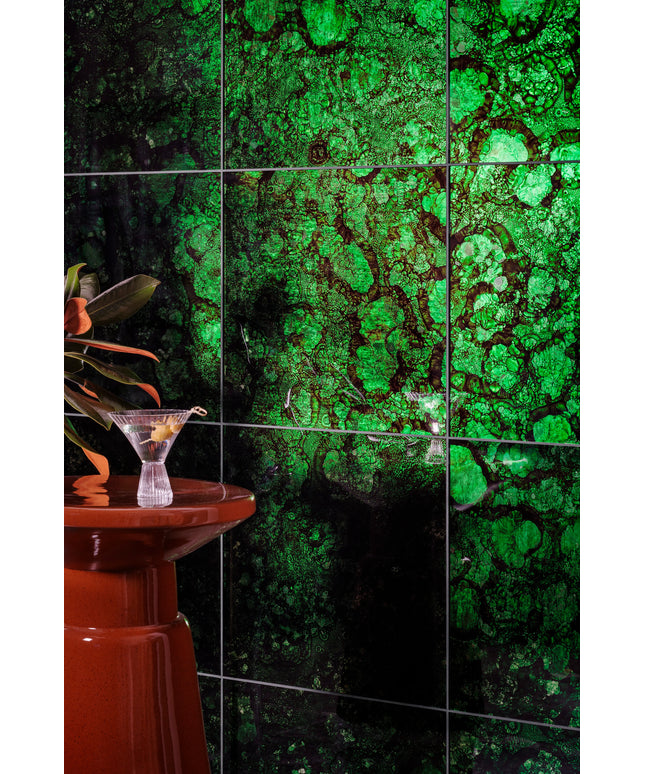 Green mottled stone-look ceramic wall tiles with dark grout lines, shown in a styled interior setting with a red pedestal and a cocktail glass.