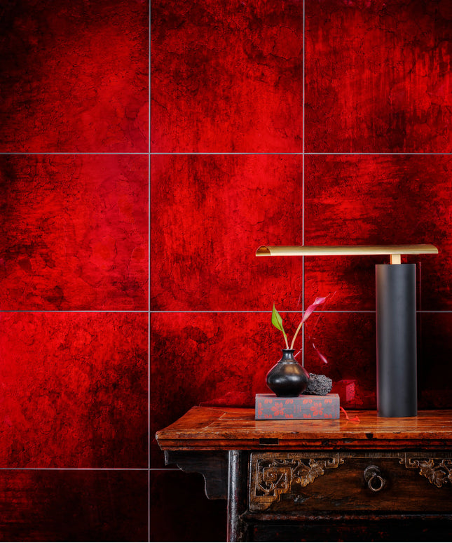 Red textured wall tiles with a glossy finish, styled in a modern interior setting behind a dark wooden console table with a black table lamp and a small vase.