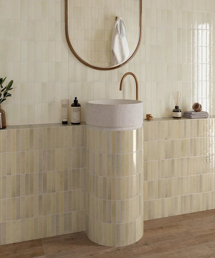 Bathroom with a pedestal sink, mirror, and decorative items on a tiled wall.
