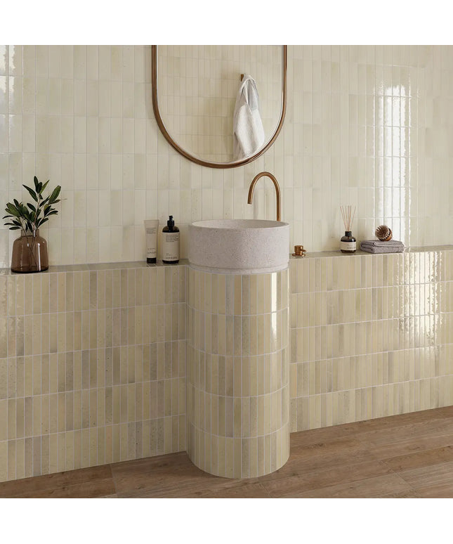 Bathroom with a pedestal sink, mirror, and decorative items on a tiled wall.