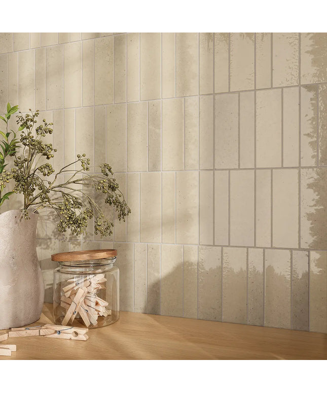 Beige rectangular subway wall tiles with a subtle distressed texture, styled on a light wood countertop next to a vase with dried greenery and a glass jar.